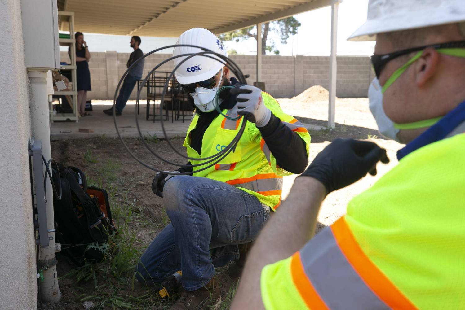 Pablo Barajas (center) and Brandon Petersen, both with Cox Communications, install internet at the Phoenix home of Tyler and Alex Palmer (background) on April 15, 2020. Cox Communications installers have changed how they do their jobs and avoid entering customers' homes in almost all situations because of the new coronavirus pandemic. The Palmers moved into their home in mid-March and have been without internet since.Cable Internet Service Coronavirus Covid 19