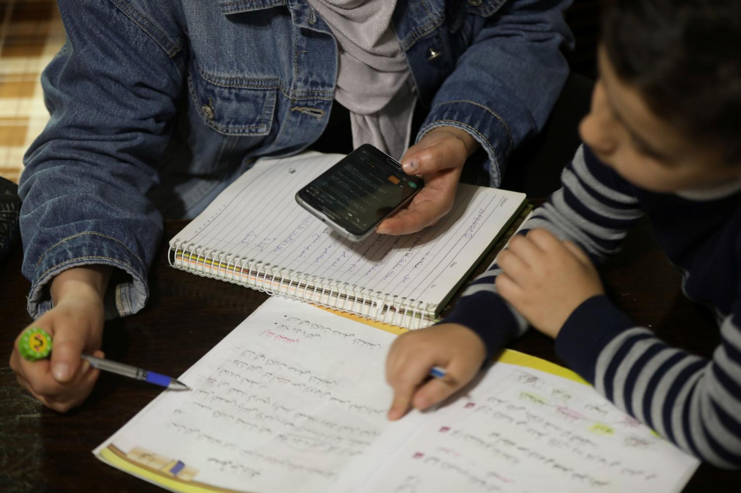 The parent of 8-year-old student Reem Al-Jaony helps her son with his school work at their home, after coronavirus lockdown forced schools to go online amid concerns over the spread of coronavirus disease (COVID-19), in Amman, Jordan March 23, 2020. Picture taken March 23, 2020. REUTERS/Muhammad Hamed
