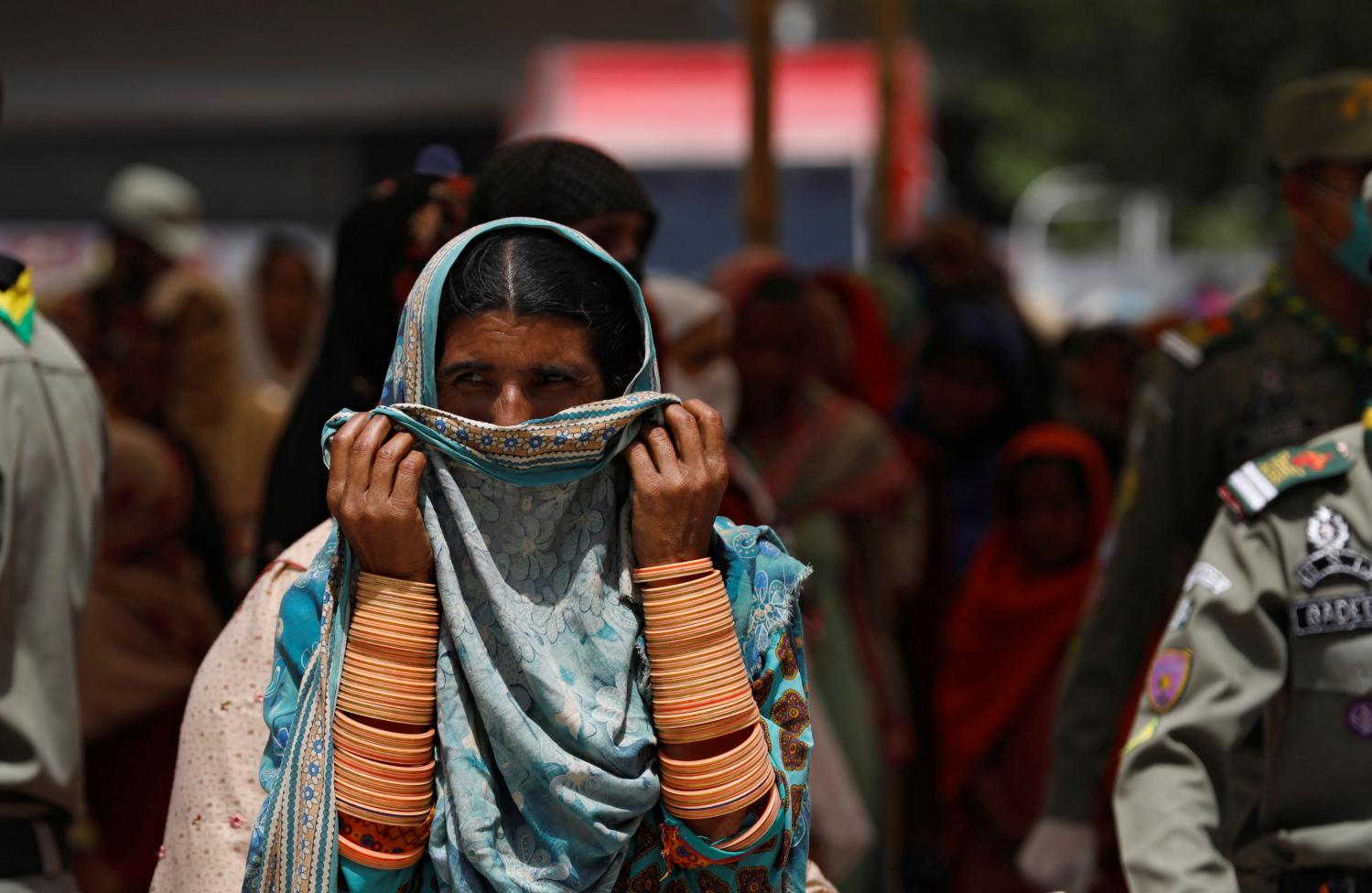 A woman covers her nose and mouth with ? scarf, as she along with others waits to receive cash from a country-wide Ehsaas Emergency Cash program, introduced by the government for vulnerable families due to the ongoing spread of coronavirus disease (COVID-19), in Karachi, Pakistan April 11, 2020. REUTERS/Akhtar Soomro
