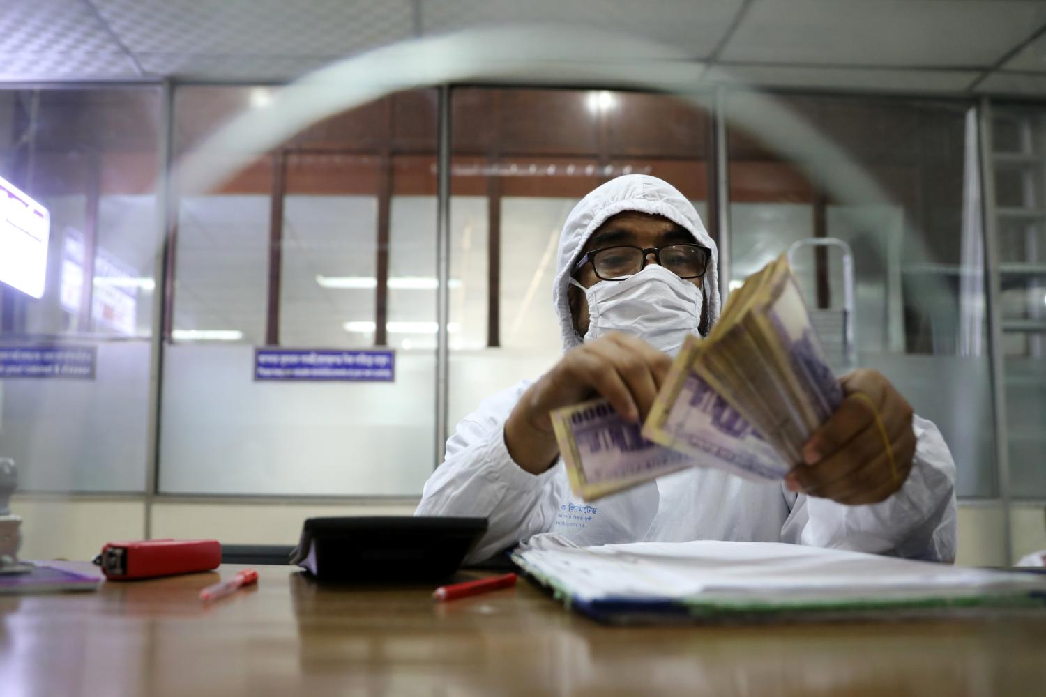 A government bank employee wears a protective suit while counting money amid the coronavirus disease (COVID-19) outbreak in Dhaka, Bangladesh, April 2, 2020. REUTERS/Mohammad Ponir Hossain