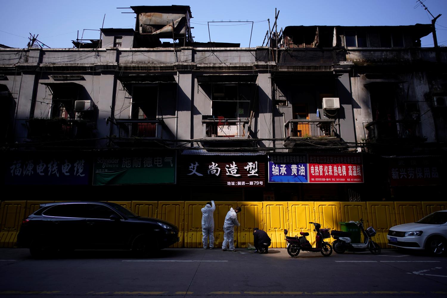 Workers in protective suits repair barriers that have been built to separate residential buildings from a street in Wuhan, capital of Hubei province and China's epicentre of the novel coronavirus disease (COVID-19) outbreak, April 12, 2020. REUTERS/Aly Song