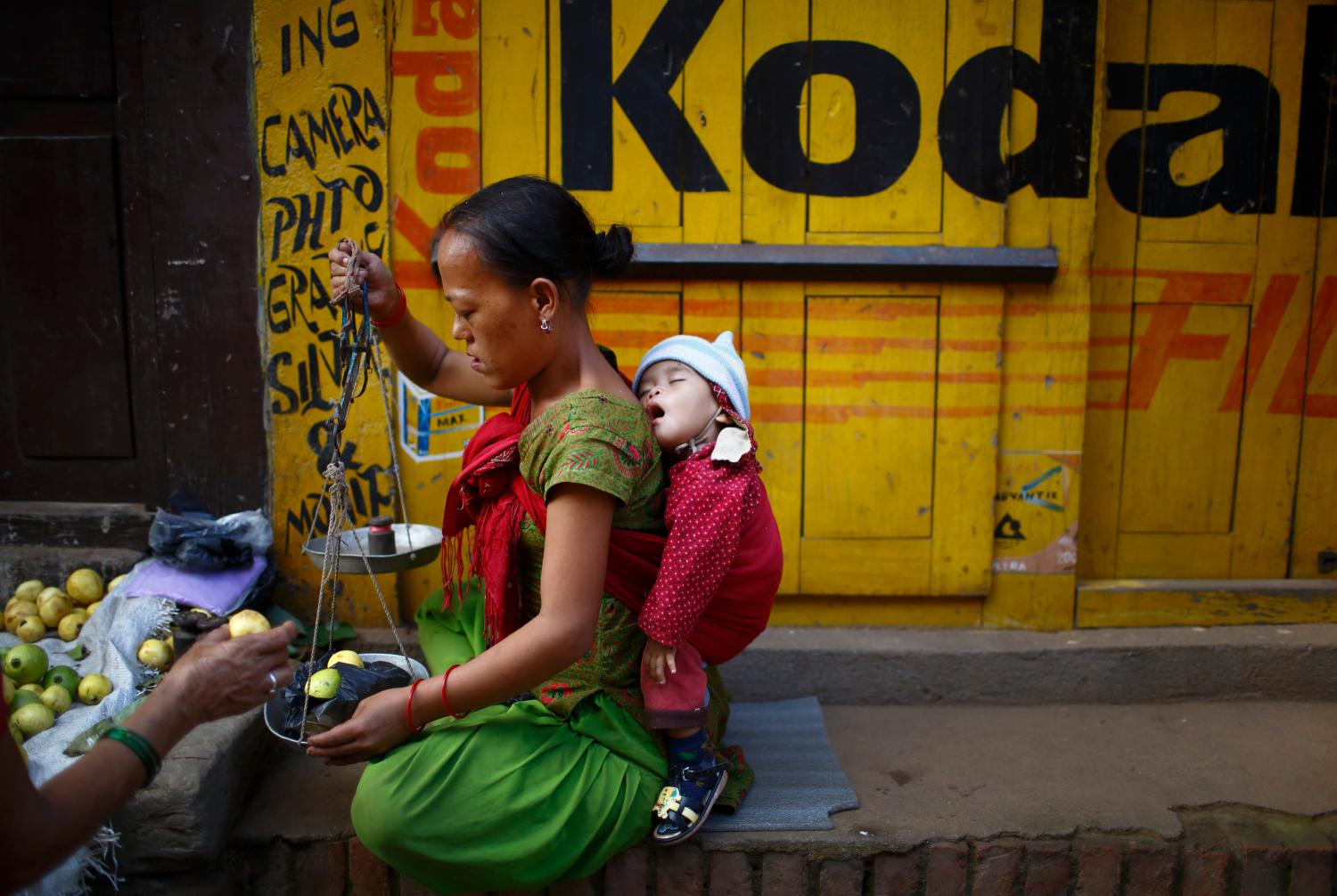 A child sleeps on the back of her mother as she sells fruits to customers along the streets in the ancient city of Bhaktapur, near Nepal's capital Kathmandu September 23, 2013. REUTERS/Navesh Chitrakar (NEPAL - Tags: SOCIETY)