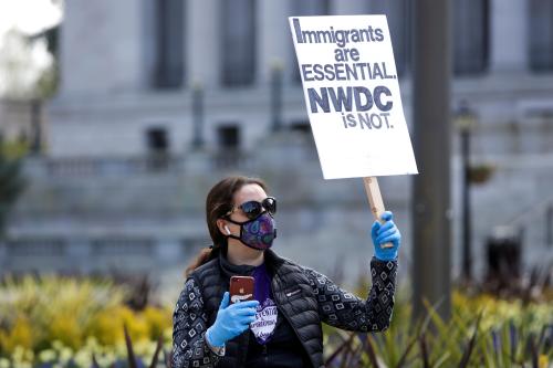Tae Phoenix of Seattle holds a sign referring to the Northwest Detention Center in Tacoma, Washington where immigrants are held protests outside the Washington state capitol with family and others concerned about the safety and health of inmates as efforts continue to slow the spread of the coronavirus disease (COVID-19) in Olympia, Washington, U.S. April 11, 2020.  REUTERS/Jason Redmond