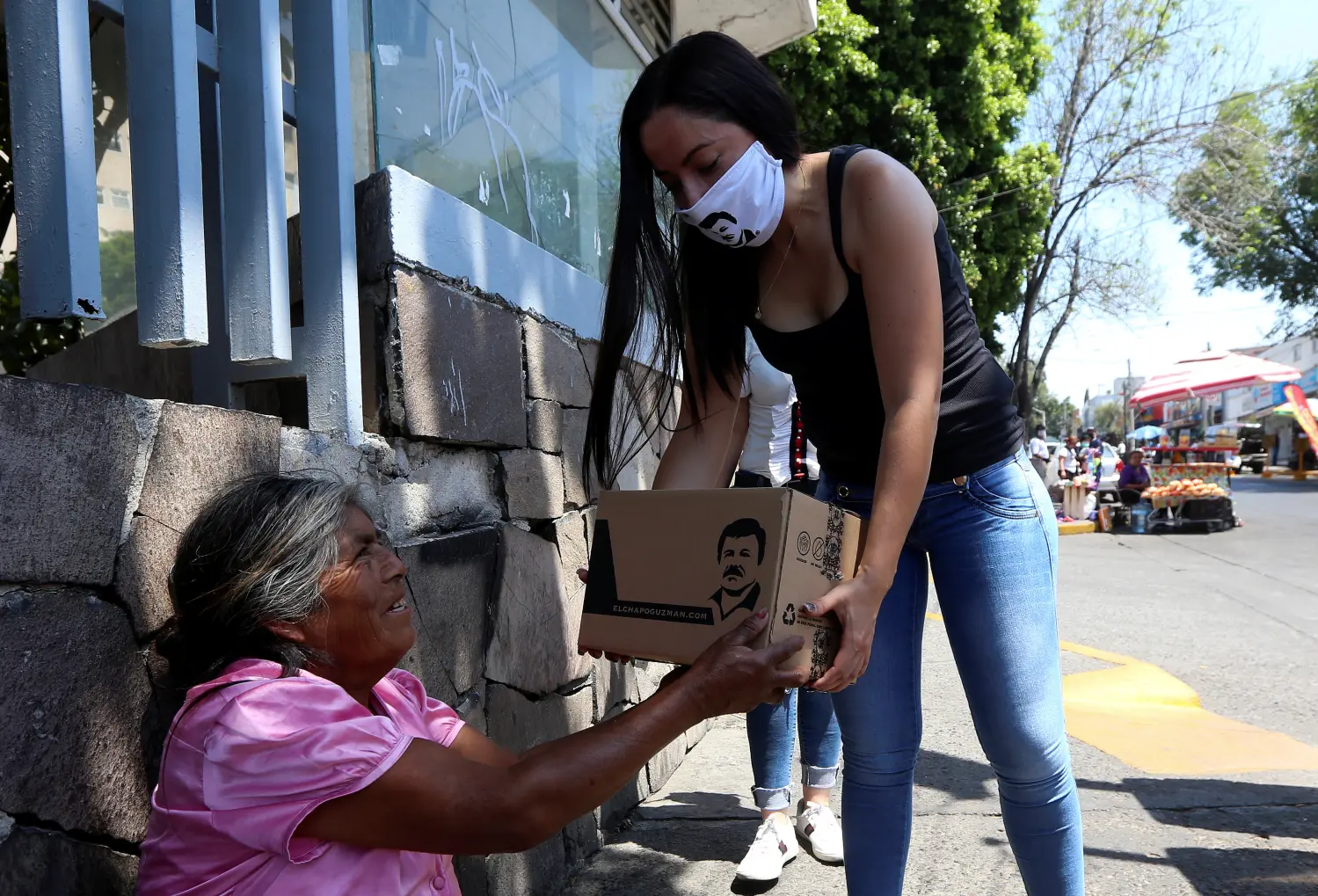 An employee of the clothing brand "El Chapo 701", owned by Alejandrina Gisselle Guzman, daughter of the convicted drug kingpin Joaquin "El Chapo" Guzman, hands out a box with food, face masks and hand sanitizers to an elderly woman as part of a campaign to help cash-strapped elderly people during the coronavirus disease (COVID-19) outbreak, in Guadalajara, Mexico April 16, 2020. The number 701 refers to the 2009 World's Billionaires ranking given by Forbes magazine to Mexican drug lord Joaquin "El Chapo" Guzman. REUTERS/Fernando Carranza