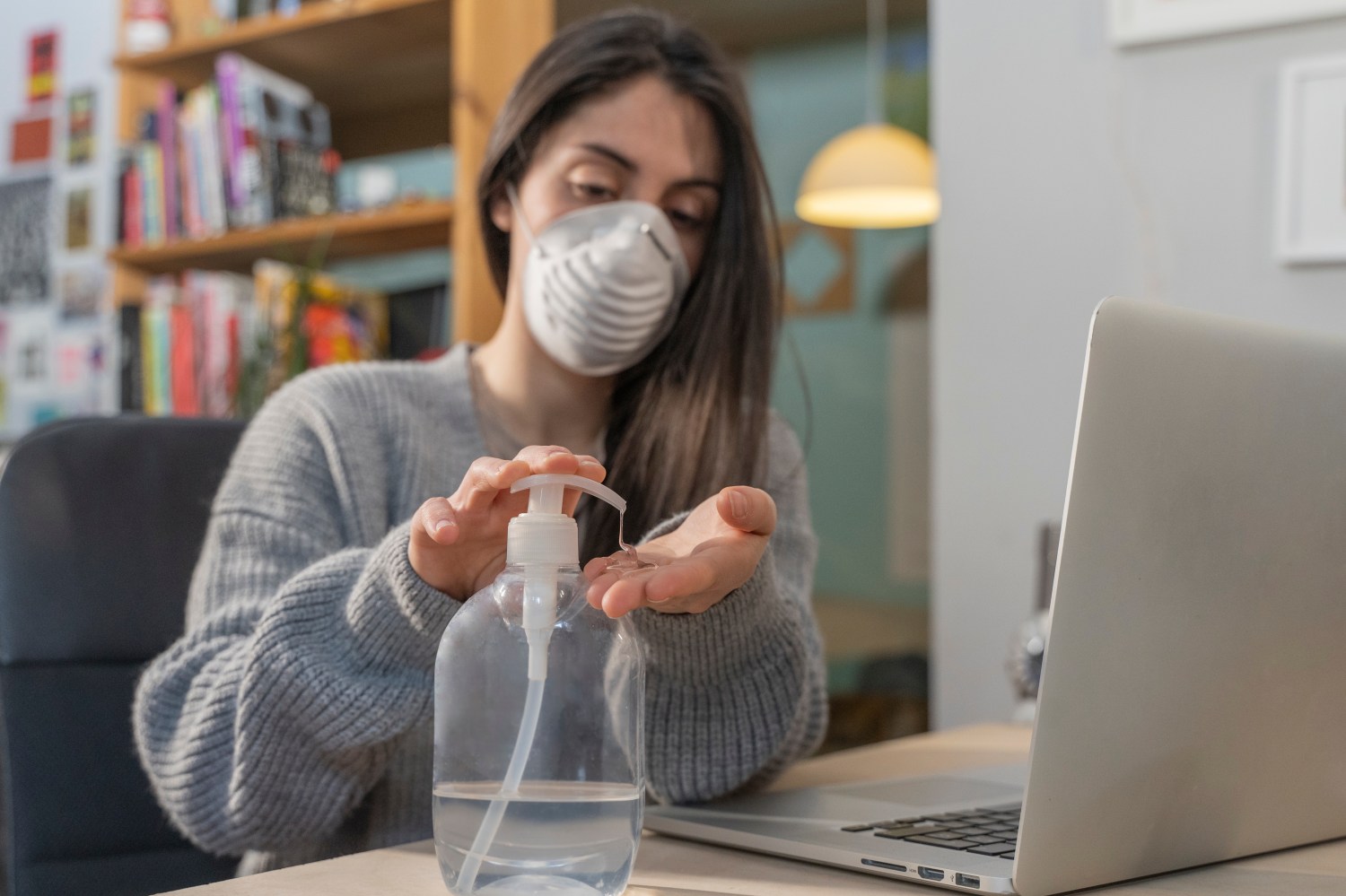 Coronavirus. Business woman working from home wearing protective mask. Business woman in quarantine for coronavirus wearing protective mask. Working from home. Cleaning her hands with sanitizer gel.