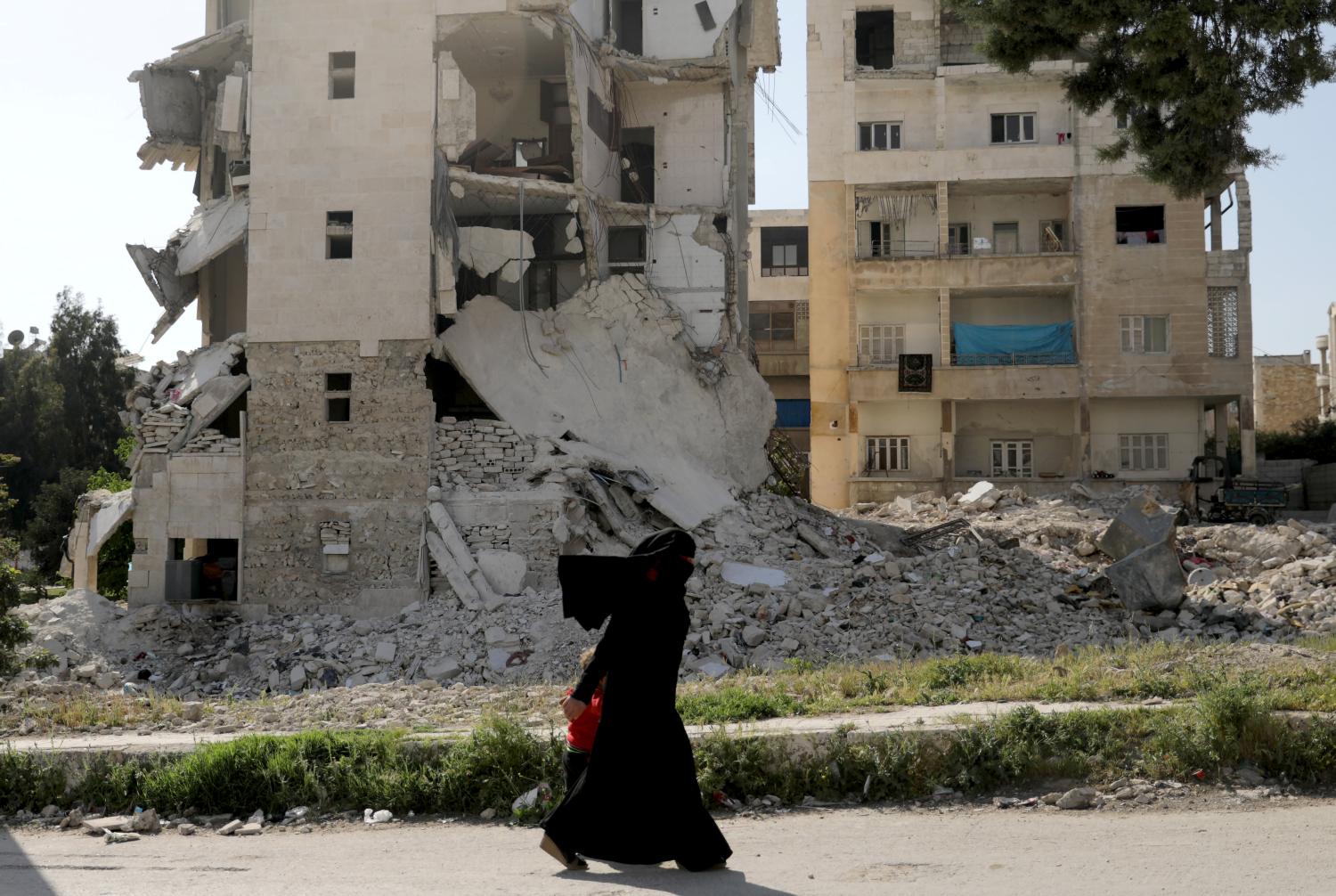 A woman walks past damaged buildings with her child in the rebel-held Idlib city, Syria April 19, 2020. Picture taken April 19, 2020.  REUTERS/Khalil Ashawi