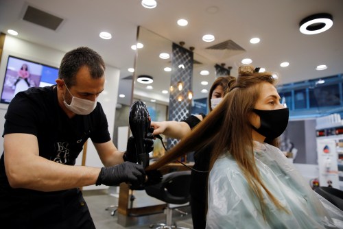 Hairdresser Oguz Kutlu gives hair treatment to his customer Elena Kuznetsova, both wearing protective masks, on the first day of the reopening of his hair salon which was closed since March 21 amid the spread of the coronavirus disease (COVID-19), in Istanbul, Turkey, May 11, 2020. REUTERS/Umit Bektas