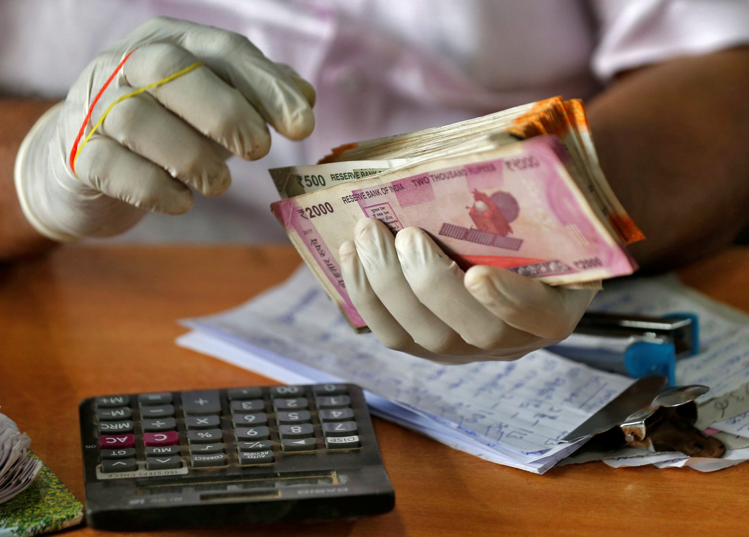 A trader wearing protective hand gloves counts Indian currency notes at a market during a 21-day nationwide lockdown to limit the spreading of coronavirus disease (COVID-19), in Kochi, India, March 27, 2020. REUTERS/Sivaram V