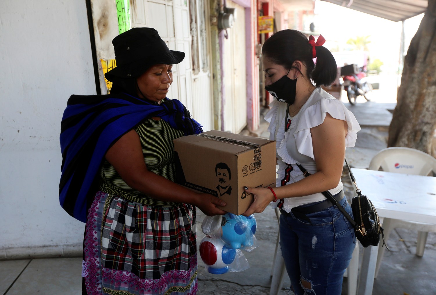 An employee of the clothing brand "El Chapo 701", owned by Alejandrina Gisselle Guzman, daughter of the convicted drug kingpin Joaquin "El Chapo" Guzman, hands out a box with food, face masks and hand sanitizer to an elderly woman as part of a campaign to help cash-strapped elderly people during the coronavirus disease (COVID-19) outbreak, in Guadalajara, Mexico April 16, 2020. The number 701 refers to the 2009 World's Billionaires ranking given by Forbes magazine to Mexican drug lord Joaquin "El Chapo" Guzman. REUTERS/Fernando Carranza