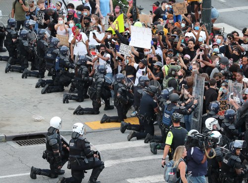 In a show of peace and solidarity, law enforcement officials with riot shields take a knee before protesters during a fourth day of protests over the death of George Floyd on Monday, June 1, 2020, in Atlanta. Photo by Curtis Compton/Atlanta Journal-Constitution/TNS/ABACAPRESS.COM