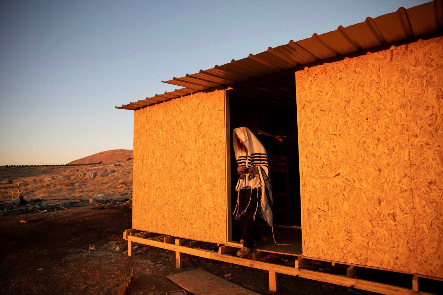 A Jewish settler wearing a Jewish prayer shawl stands at the entrance to a temporary structure in the Jewish settler outpost of Maoz Ester in the Israeli-occupied West Bank June 23, 2020. REUTERS/Ronen Zvulun     TPX IMAGES OF THE DAY