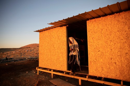 A Jewish settler wearing a Jewish prayer shawl stands at the entrance to a temporary structure in the Jewish settler outpost of Maoz Ester in the Israeli-occupied West Bank June 23, 2020. REUTERS/Ronen Zvulun     TPX IMAGES OF THE DAY