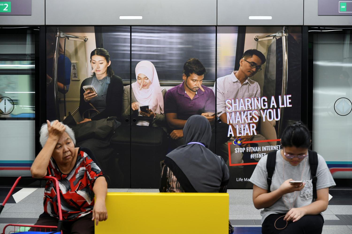 Commuters sit in front of an advertisement discouraging the dissemination of fake news, at a train station in Kuala Lumpur, Malaysia March 28, 2018. Picture taken March 28, 2018. REUTERS/Stringer