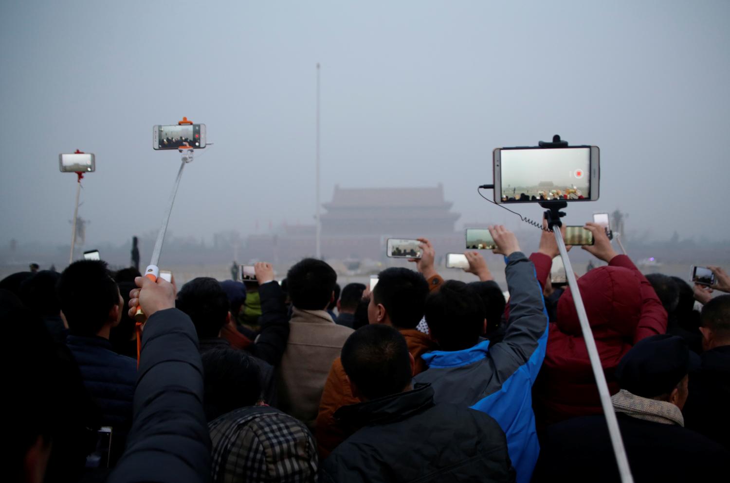 People take videos of a flag-raising ceremony during smog at Tiananmen Square after a red alert was issued for heavy air pollution in Beijing, China, December 20, 2016. REUTERS/Jason Lee