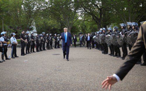 A White House staff member gestures to move the press corps back as U.S. President Donald Trump walks between lines of riot police for a photo opportunity at St John's Church during ongoing protests over racial inequality in the wake of the death of George Floyd while in Minneapolis police custody, near the White House in Washington, U.S., June 1, 2020. REUTERS/Tom Brenner