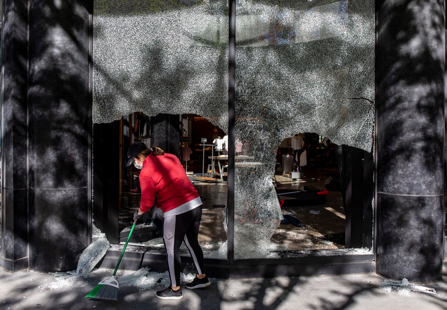 Volunteer Julie Bunna sweeps broken glass along Michigan Avenue in front of the ransacked Under Armour store Sunday, May 31, 2020, the morning after protests led to widespread destruction in downtown Chicago. (Brian Cassella/Chicago Tribune/TNS)