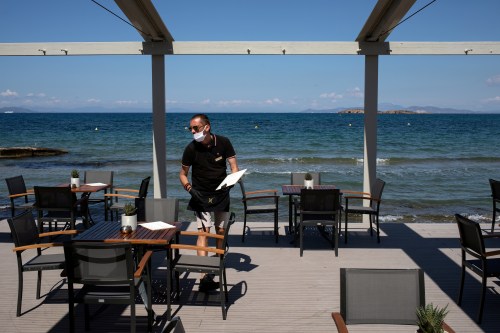 FILE PHOTO: An employee wearing a protective mask, leaves a menu on a table at the beach bar of the Divani Apollon Palace hotel, on the first day of the opening of hotels in Greece, following a nationwide lockdown against the spread of the coronavirus disease (COVID-19), in Athens, Greece, June 1, 2020. REUTERS/Alkis Konstantinidis/File Photo