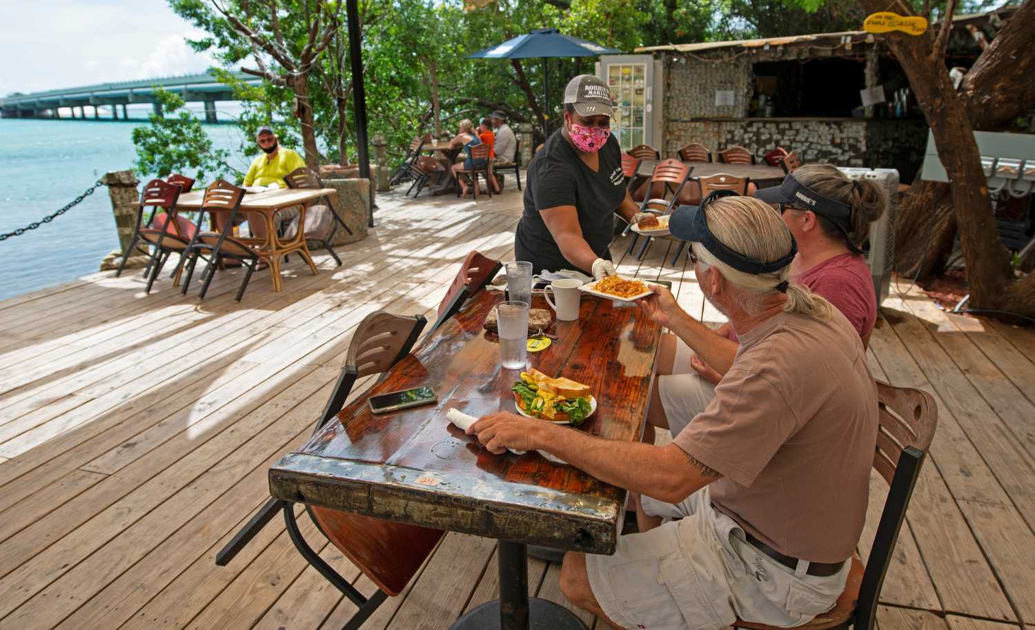 Alexeen Simms, a server at the Hungry Tarpon Restaurant in Islamorada, Fla., provides a luncheon entree to a couple Monday. June 1. 2020. After being closed to visitors since March 22, 2020, to help curtail the spread of coronavirus disease (COVID-19), the Florida Keys reopened to tourists Monday.  Andy Newman/Florida Keys News Bureau/Handout via REUTERS    ATTENTION EDITORS - THIS IMAGE HAS BEEN SUPPLIED BY A THIRD PARTY.