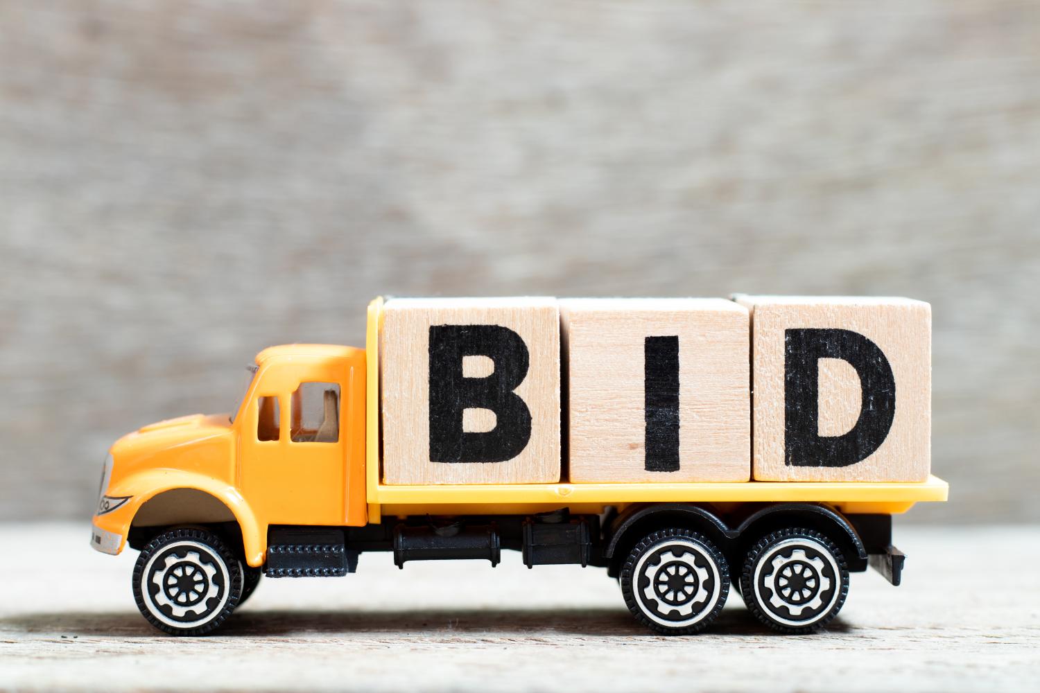 Truck hold letter block in word bid on wood background