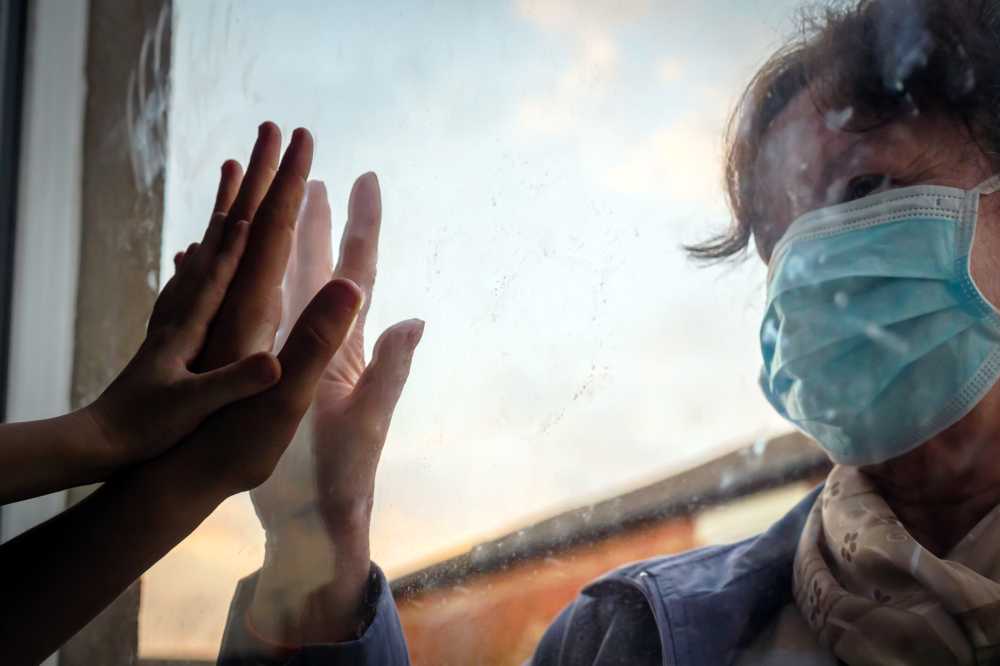 People touching hands through glass with COVID mask