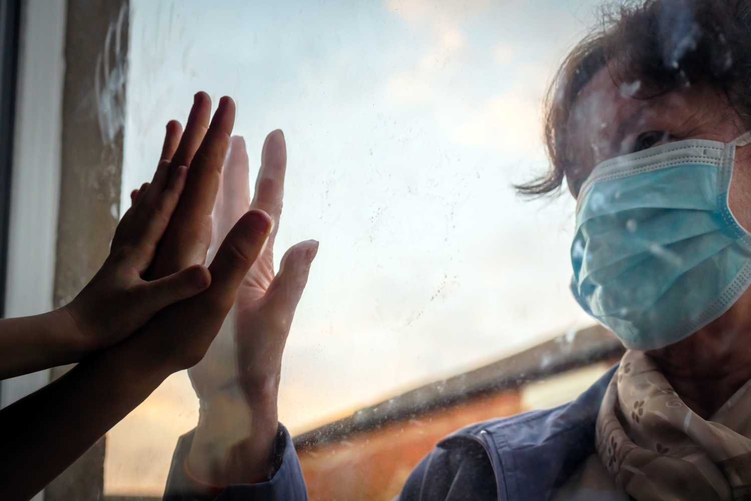 People touching hands through glass with COVID mask