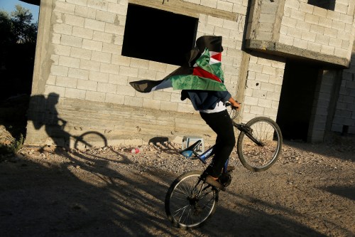 A boy covered with a Palestinian flag rides a bicycle during a protest against Israel's plan to annex parts of the Israeli-occupied West Bank, in the Palestinian village of Bardala in the northern Jordan Valley June 27, 2020. REUTERS/Raneen Sawafta