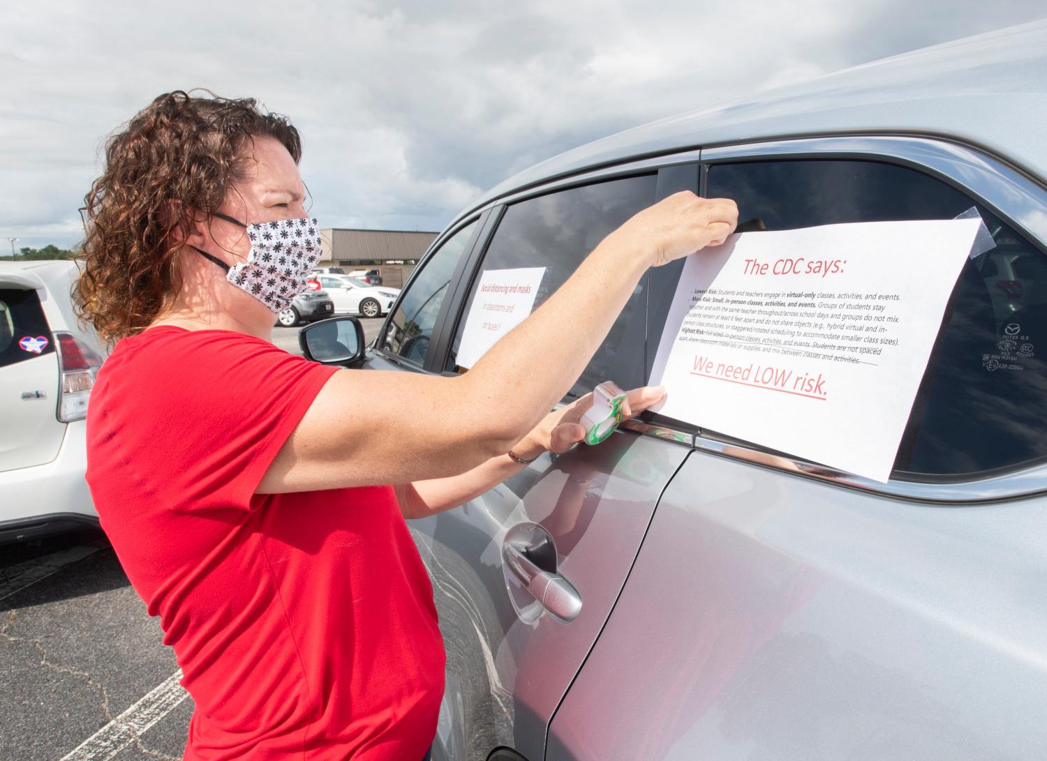 Debbie Springer, an educator and parent, tapes signs on her vehicle before fellow educators and parents begin their "Car Parade for the Safe Reopening of Schools" in Pensacola on Thursday, July 16, 2020.  While they are eager to get back to the classrooms, they are calling for safe conditions before doing so.Teacher Car Parade