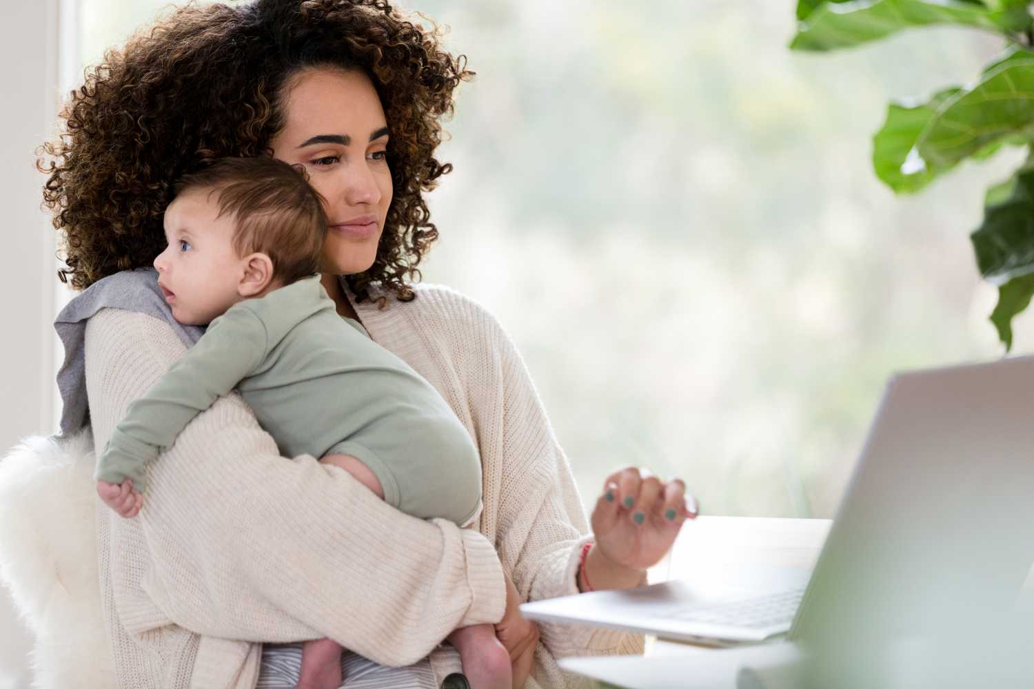 Working mom uses a laptop while holding her baby boy.