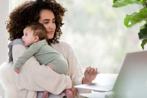 Working mom uses a laptop while holding her baby boy.