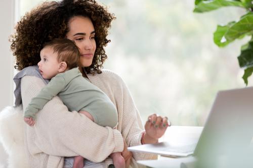 Working mom uses a laptop while holding her baby boy.