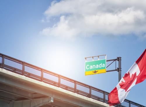 Destination Canada sign on highway with Canadian flag waving beside