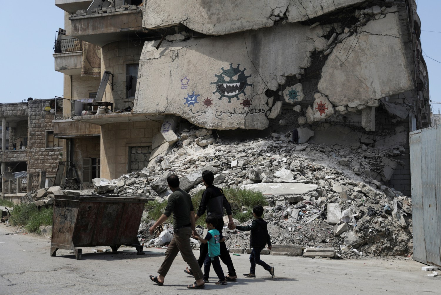 People walk past a damaged building depicting drawings alluding to the coronavirus and encouraging people to stay at home, in the rebel-held Idlib city, amid concerns about the spread of the coronavirus disease (COVID-19), Syria April 18, 2020. REUTERS/Khalil Ashawi     TPX IMAGES OF THE DAY