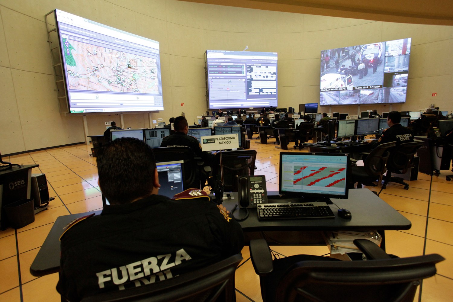 Police officers in Mexico monitor feeds from surveillance cameras displayed on several large monitors.