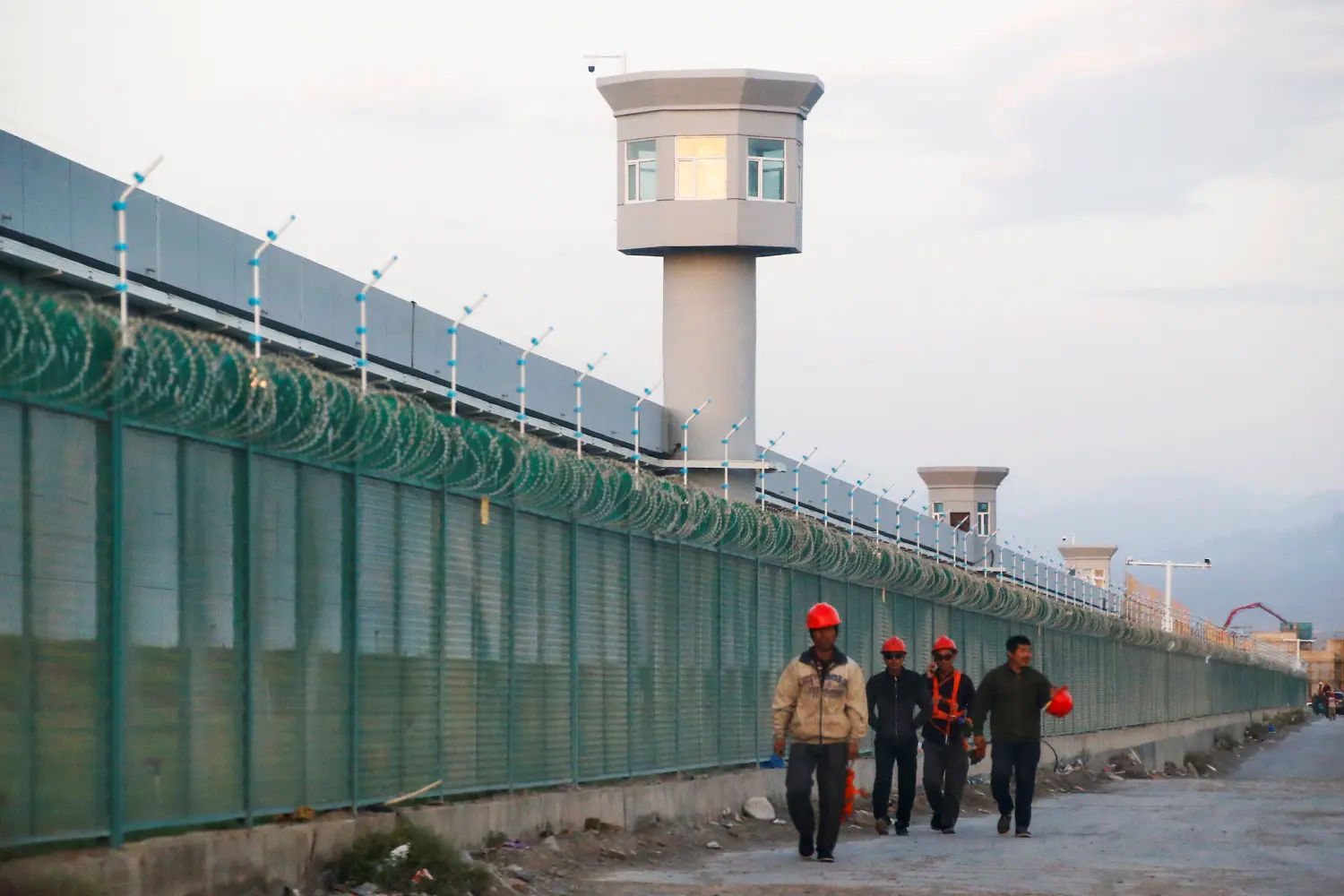 Workers walk by the perimeter fence of what is officially known as a vocational skills education centre in Dabancheng in Xinjiang Uighur Autonomous Region, China September 4, 2018. This centre, situated between regional capital Urumqi and tourist spot Turpan, is among the largest known ones, and was still undergoing extensive construction and expansion at the time the photo was taken. Picture taken September 4, 2018. To match Special Report MUSLIMS-CAMPS/CHINA REUTERS/Thomas Peter