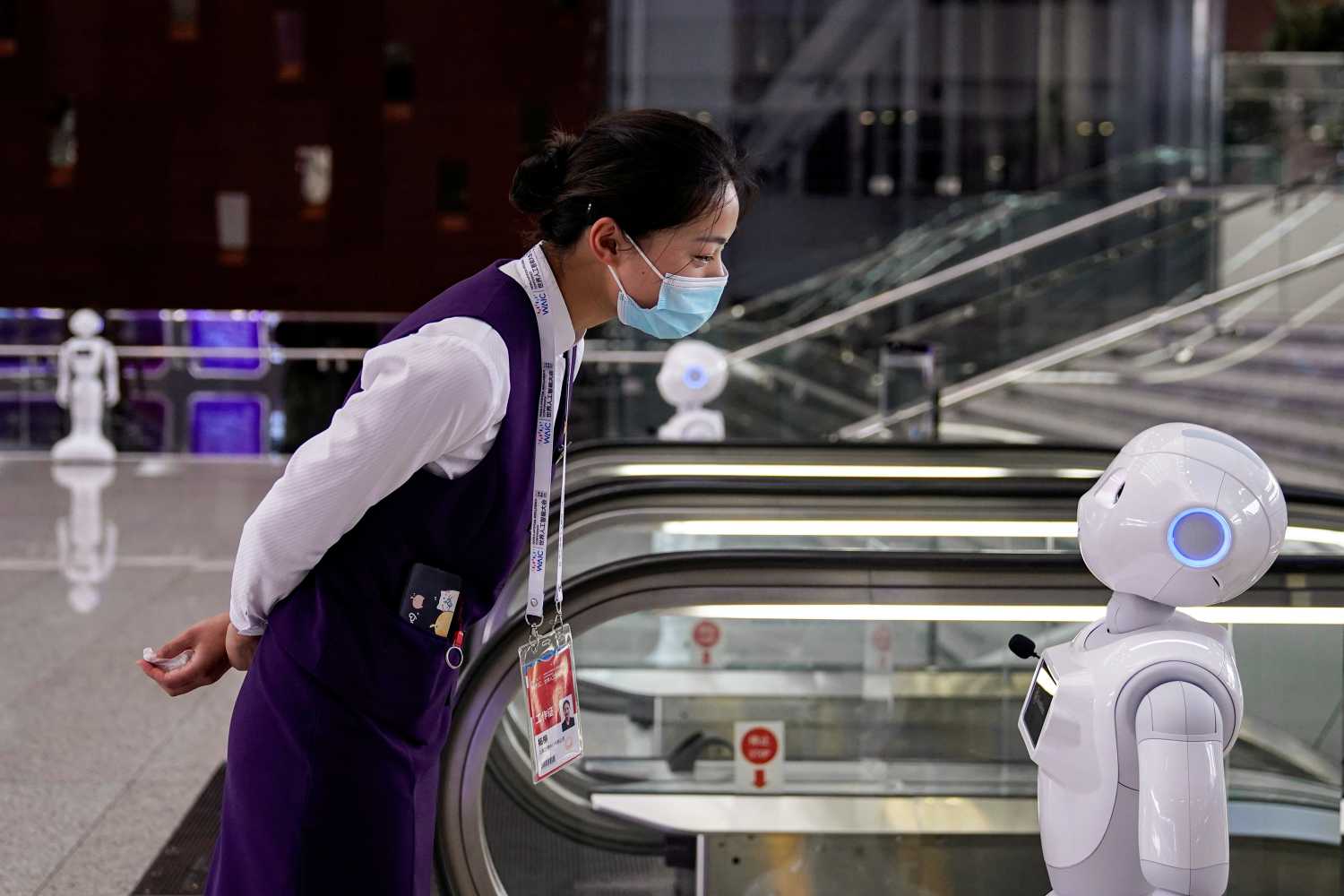 A staff member wearing a face mask following the COVID-19 outbreak looks at a robot at the venue for the World Artificial Intelligence Conference in Shanghai, China on July 9, 2020.