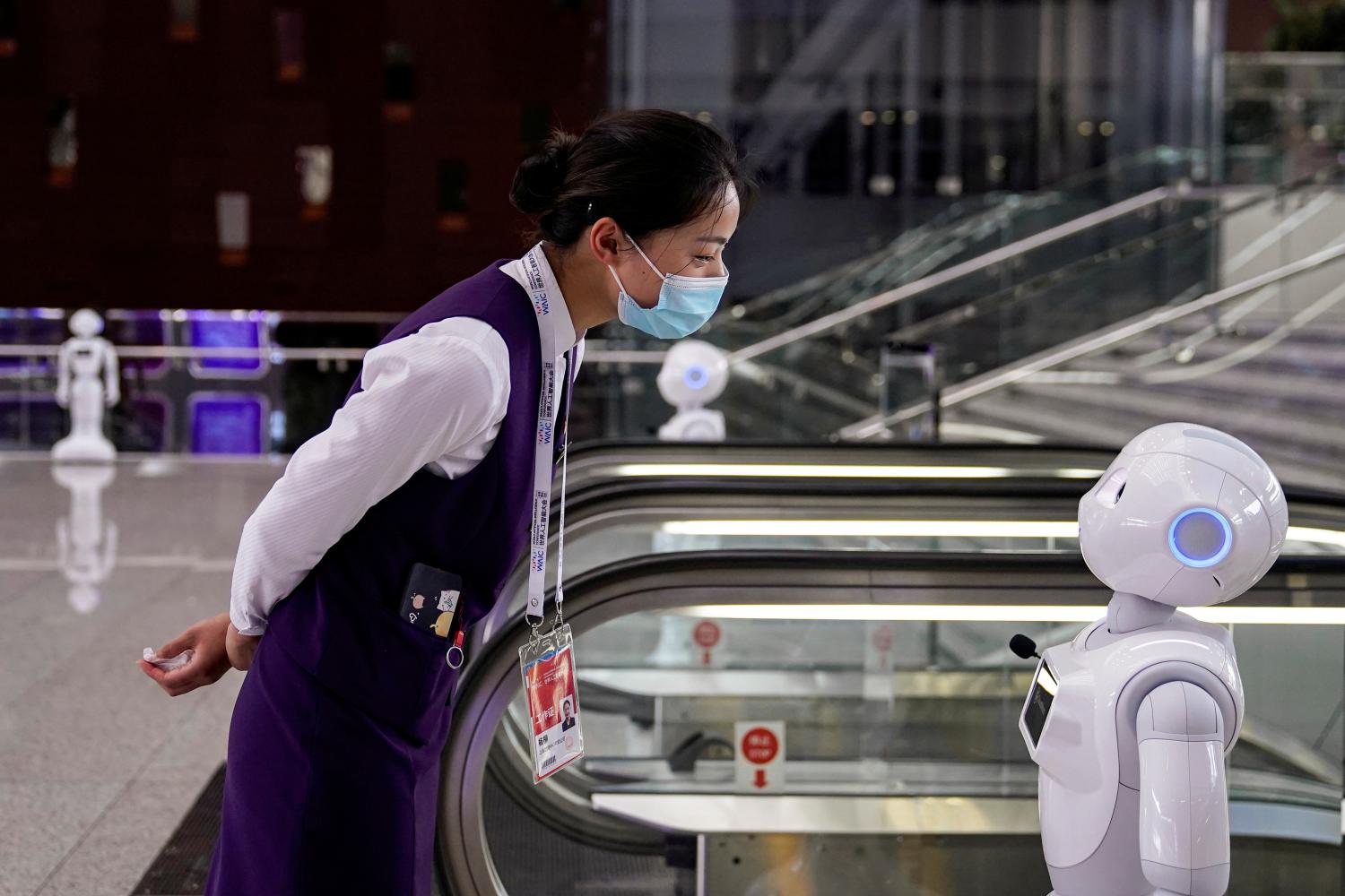 A staff member wearing a face mask following the COVID-19 outbreak looks at a robot at the venue for the World Artificial Intelligence Conference in Shanghai, China on July 9, 2020.