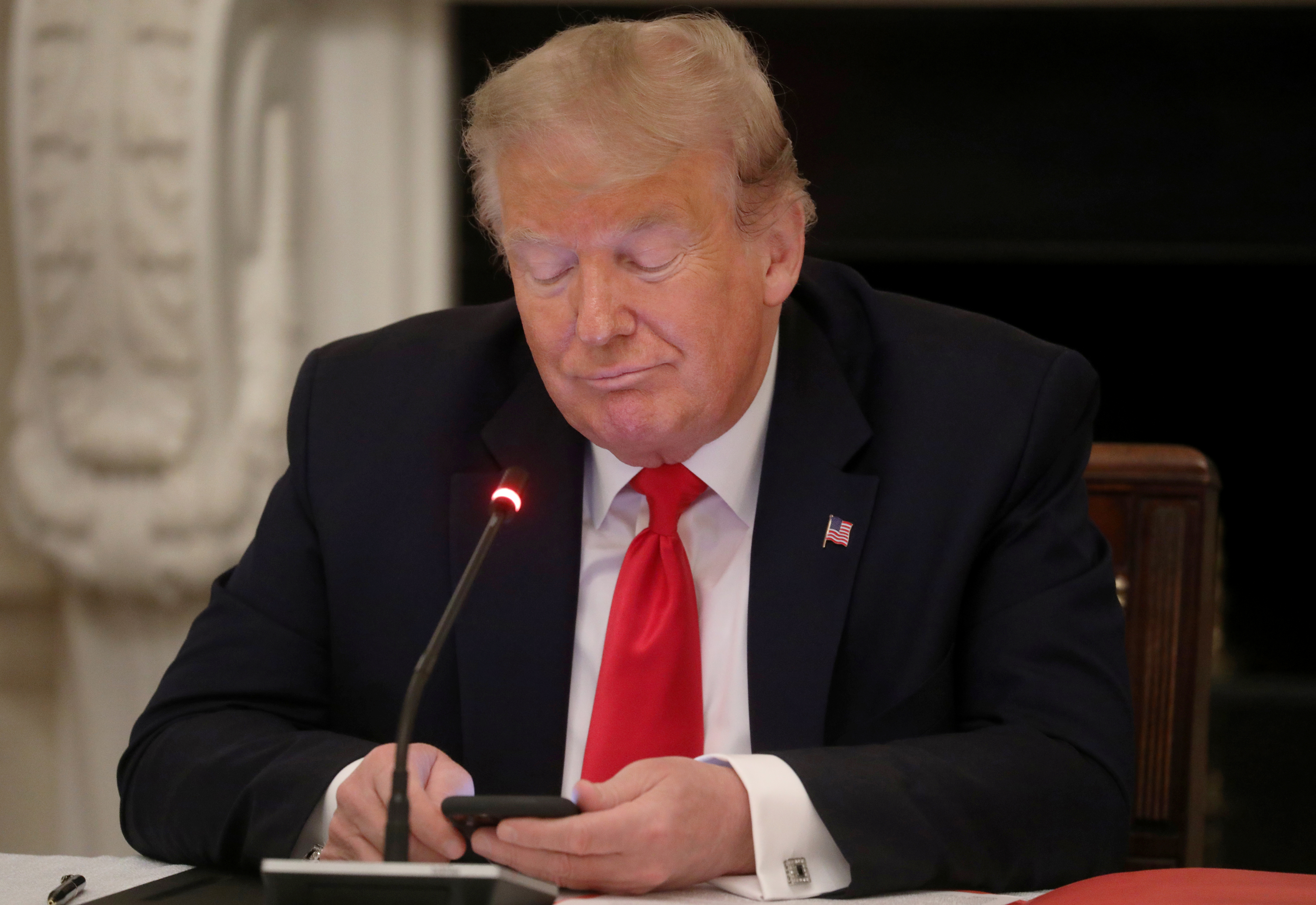 U.S. President Donald Trump is using a mobile phone during a roundtable discussion on the reopening of small businesses in the State Dining Room at the White House in Washington, U.S., June 18, 2020. REUTERS/Leah Millis