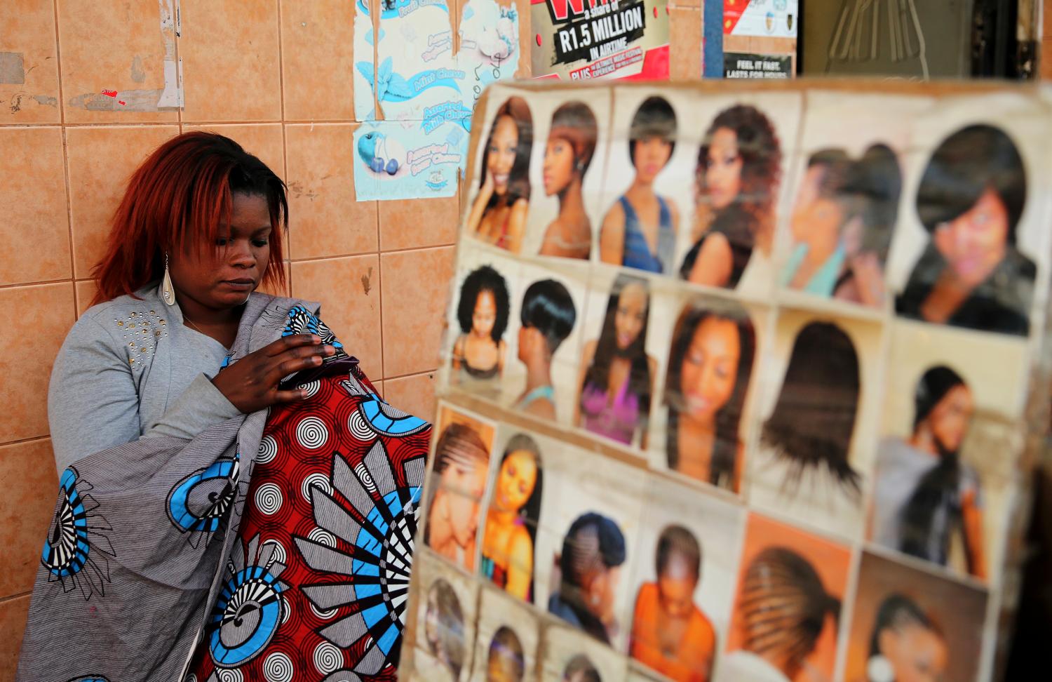 A hairdresser uses her phone as she waits for clients at a makeshift saloon in Soweto, August 4, 2014. While still largely based in the informal economy, the African haircare business has become a multi-billion dollar industry that stretches to China and India and has drawn global giants such as L'Oreal and Unilever. Hairdressers are a fixture of markets and taxi ranks across Africa, reflecting both the continent's rising incomes and demand from hair-conscious women. Picture taken August 4.    REUTERS/Siphiwe Sibeko (SOUTH AFRICA - Tags: BUSINESS SOCIETY TELECOMS)