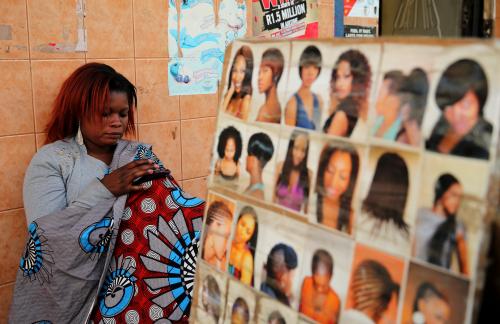 A hairdresser uses her phone as she waits for clients at a makeshift saloon in Soweto, August 4, 2014. While still largely based in the informal economy, the African haircare business has become a multi-billion dollar industry that stretches to China and India and has drawn global giants such as L'Oreal and Unilever. Hairdressers are a fixture of markets and taxi ranks across Africa, reflecting both the continent's rising incomes and demand from hair-conscious women. Picture taken August 4.    REUTERS/Siphiwe Sibeko (SOUTH AFRICA - Tags: BUSINESS SOCIETY TELECOMS)