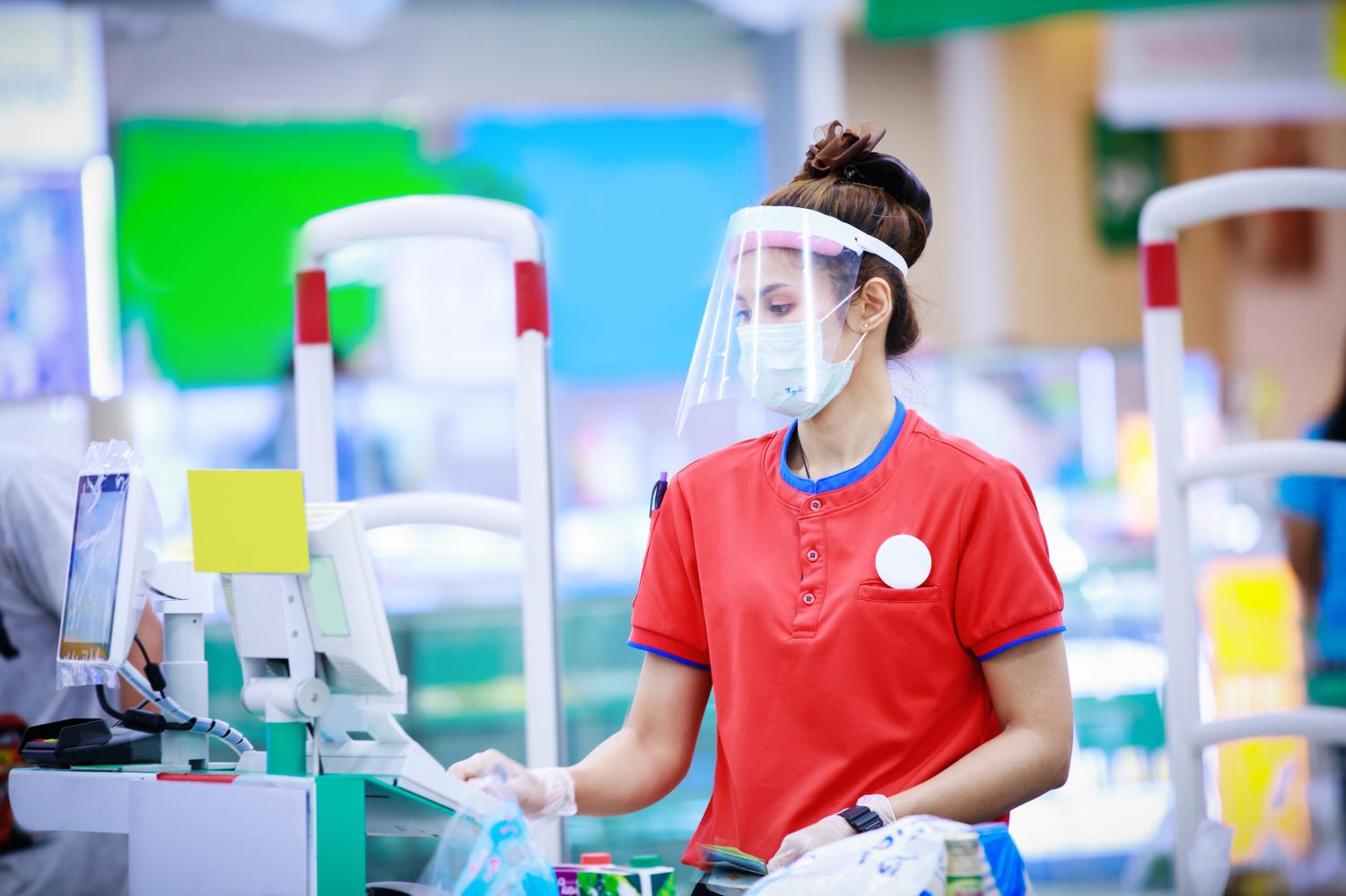 female supermarket cashier in medical protective mask and face shield working at supermarket. covid-19 spreading outbreak