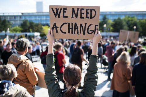 Protest scene and a woman holding a sign that reads "We need a change."