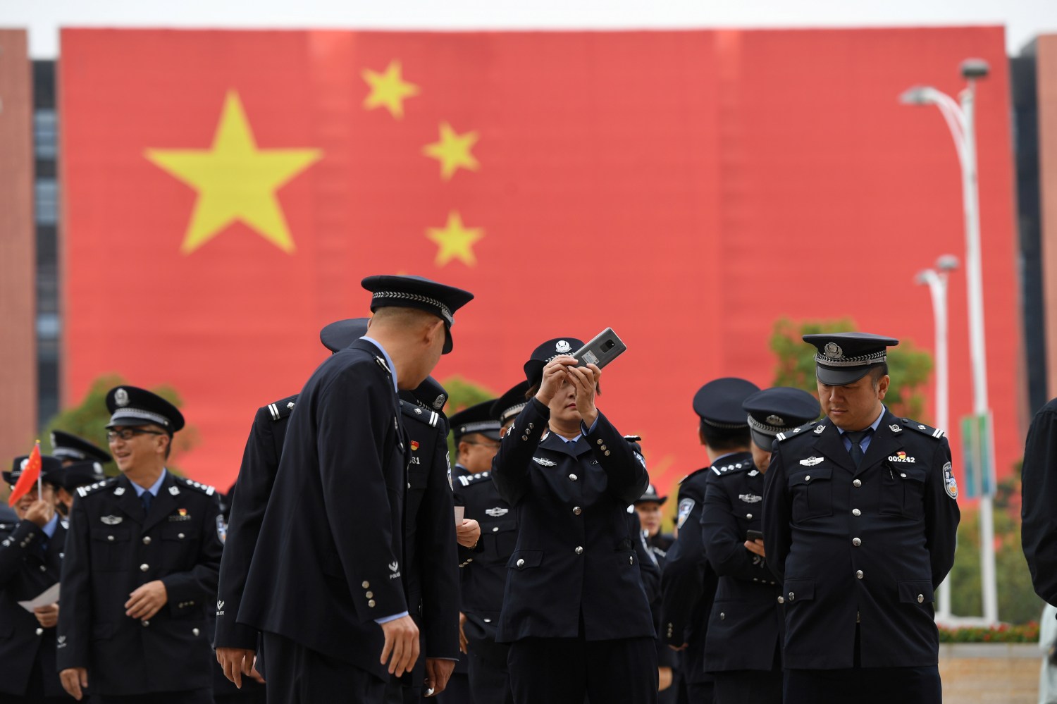 A police officer in front of a giant Chinese flag takes pictures with a mobile phone outside an exhibition marking the 70th founding anniversary of People's Republic of China, in Kunming, Yunnan province, China September 25, 2019. REUTERS/Stringer CHINA OUT.