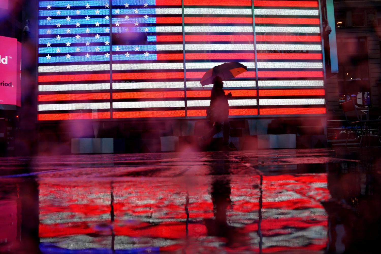A pedestrian walks in the rain past a U.S. flag displayed in Times Square in the Manhattan borough of New York City, New York, U.S., October 16, 2020. REUTERS/Carlo Allegri