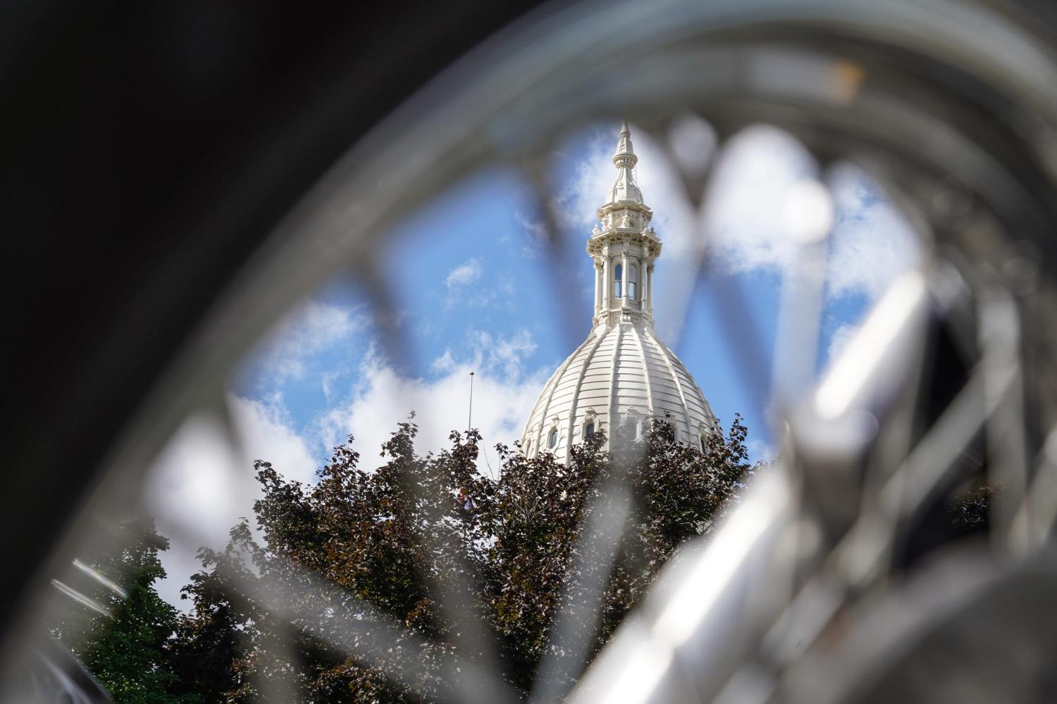 The Michigan State Capitol building is seen through the spokes of a motorcycle during the ABATE of Michigan Annual Freedom Rally outside of the Michigan State Capitol building in Lansing on Sept. 29, 2020. Bikers gathered to speak on behalf of motorcyclists who want changes to the recent auto insurance reform law that puts motorcyclists at a disadvantage.