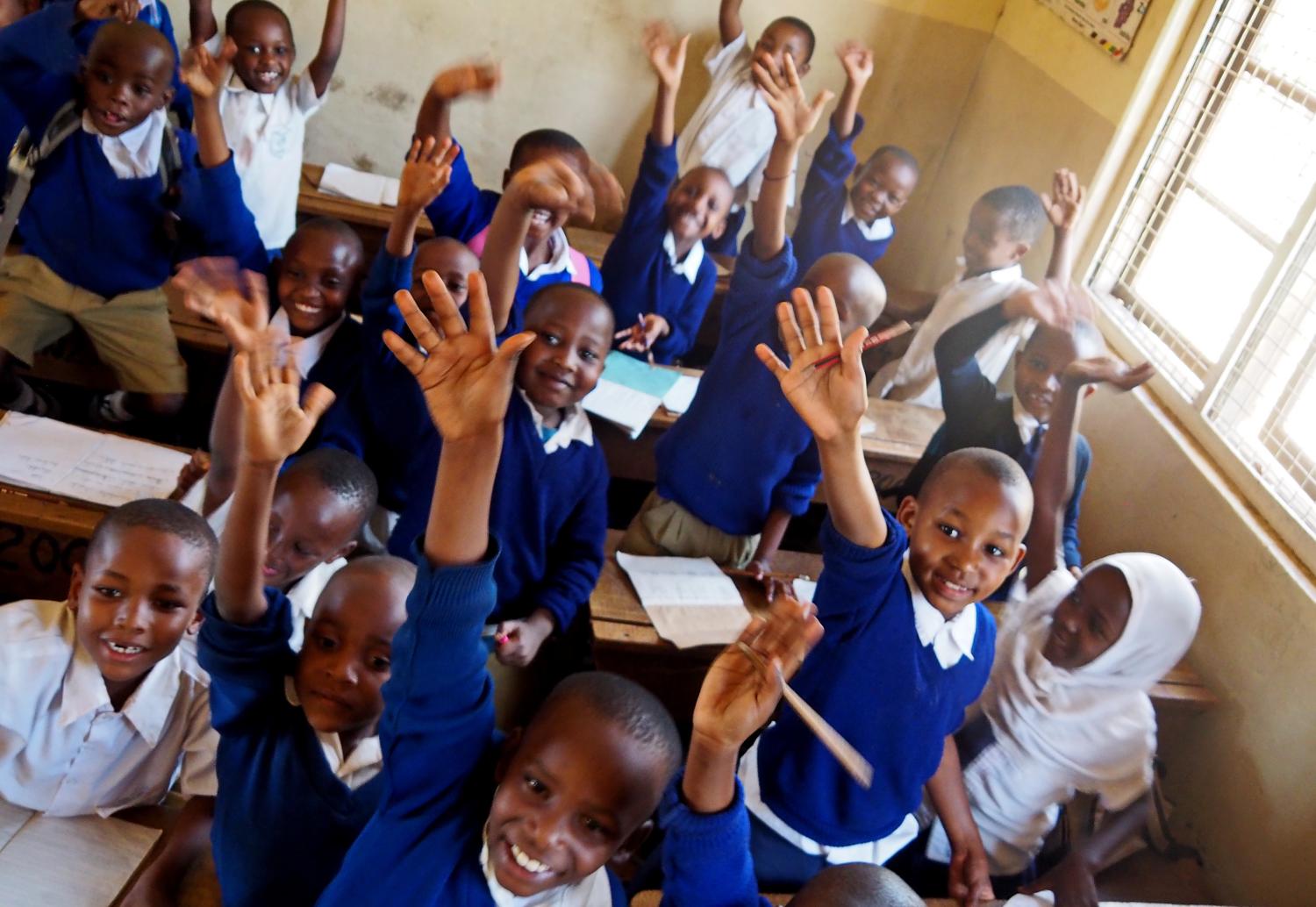 Moshi, Kilimanjaro / Tanzania - 10.06.2015: African children in a class at the Mawenzi Municipal Primary School raise their hands to answer the teacher's question.