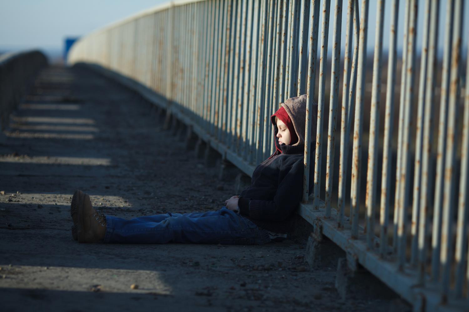 Young boy sleeping against a metal fence.