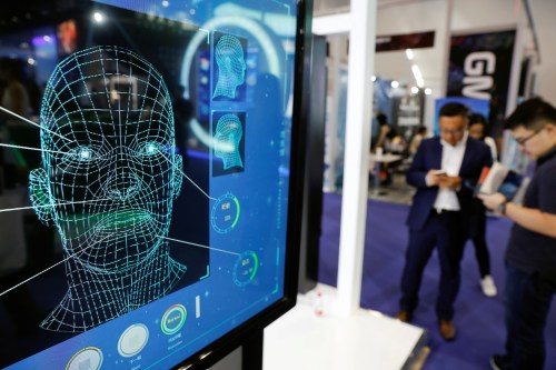 Visitors check their phones behind the screen advertising facial recognition software during Global Mobile Internet Conference (GMIC) at the National Convention in Beijing, China April 27, 2018. REUTERS/Damir Sagolj