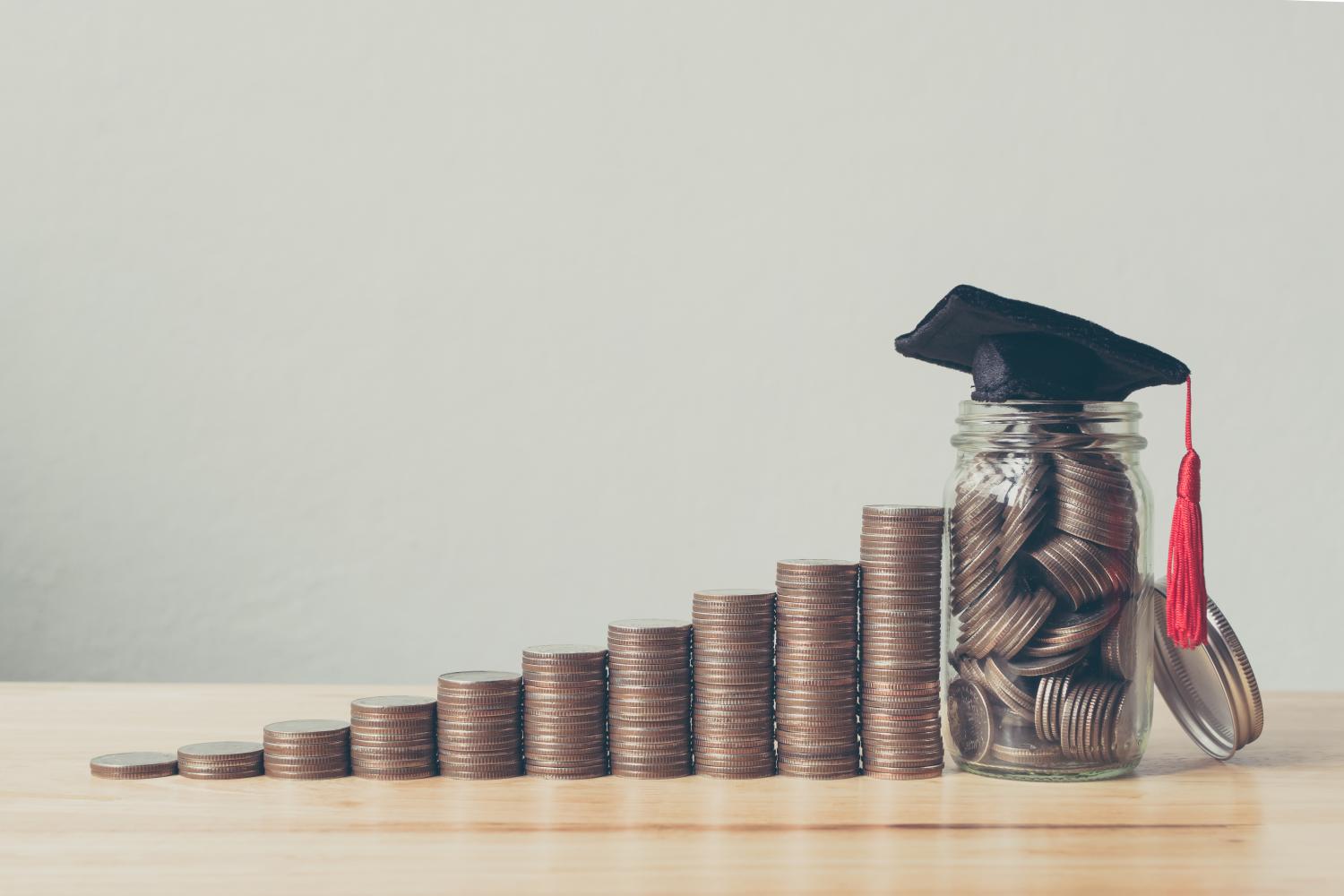 Piles of coins with a graduation cap on the tallest pile.