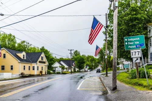 Blue Hill, USA - June 9, 2017: American flag on city main street in Maine during rainy cloudy weather with directions