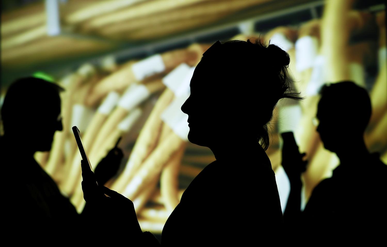 People in silhouette look at their mobile phones with cables from an internet switching station projected in the background.